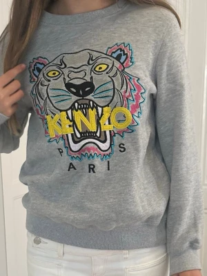 Grå Kenzo sweatshirt med tigertryck - Snygg grå sweatshirt från Kenzo med färgglad tigerhuvud. Bra skick. Behöver sälja den för att den har blivit för liten for mig. 🥰Storlek M men passar XS/S
