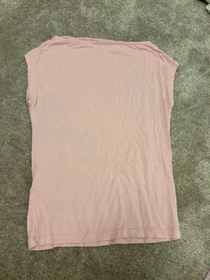 Ljusrosa ärmlös topp - En enkel och stilren ljusrosa topp i mjukt material. Toppen är ärmlös med rund halsringning och har en rak passform. Perfekt att matcha med jeans eller kjol för en avslappnad look.