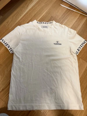 Vit Valentino t-shirt med logga - Pris kan diskuteras, Snygg vit t-shirt från Valentino med svart logga på bröstet och textdetaljer på ärmar och krage. Klassisk passform och tillverkad i mjuk bomull som känns skön mot huden. Perfekt för dig som gillar stilrena plagg med exklusiv känsla. 