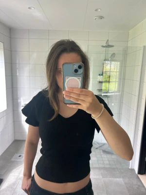 Svart ribbad topp med v-ringning - Snygg svart ribbad topp med v-ringning och korta, volangiga ärmar. Modellen är croppad och sitter tight. Stl S. Skriv vid frågor💕