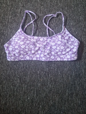 Lila blommig bikiniöverdel - Superfin bikiniöverdel i lila med vitt blommönster och smala axelband. Perfekt för sommardagar på stranden eller vid poolen. Bekväm passform och stretchigt material som sitter snyggt. Snygg och trendig look för dig som gillar färg och mönster.