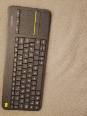 Logitech trådlöst tangentbord med touchpad - Säljer ett svart trådlöst tangentbord från Logitech med inbyggd touchpad och gul detalj. Perfekt för att styra datorn eller mediacenter från soffan. Smidig och tunn design i plast, lätt att ta med och använda överallt.