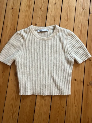 Ribbad beige topp från Zara - Superfin topp från Zara i beige färg. Modellen är en stickae topp. Säljer pågrund av att den är för liten!☺️sitter väldigt bra på!💗