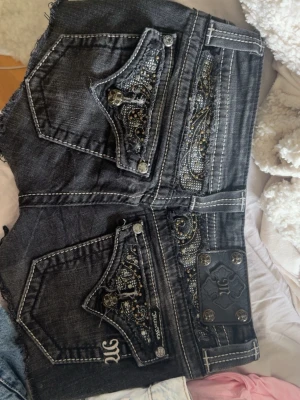 Svarta Miss Me shorts med broderi - Snygga svarta jeansshorts från Miss Me med coola broderade detaljer och nitar på bakfickorna. Dom är i storlek 26 men passar mig bra som brukar ha storlek xs! Dom är ifrån början skinnyjeans som jag har klippt av till shorts!🥰