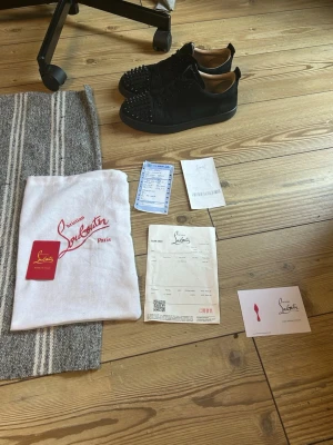 Svarta Christian Louboutin sneakers STORLEK 45 - Svarta sneakers från Christian Louboutin med mattsvart mocka och ikoniska nitar på tån. Lågt skaft, svarta skosnören och diskret röd detalj på insidan. Snygg och edgy design som sticker ut. Perfekta för dig som vill ha något unikt och lyxigt.