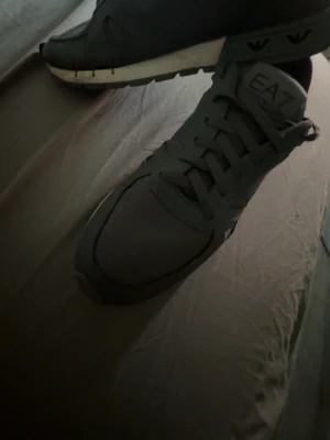 Svarta EA7 Emporio Armani sneakers - Snygga svarta sneakers från EA7 Emporio Armani med meshdetaljer och logga på sidan. Skorna har en vit sula med svarta detaljer och klassisk snörning. Perfekta för dig som gillar stilrena och sportiga skor. Storlek 43 priset är inte fast
