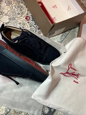 Mörkblå sneakers från Louboutin - Snygga mörkblå sneakers från Christian Louboutin med klassisk röd sula. Skorna är låga och har ovandel i mocka med matchande mörkblå skosnören. Kommer med originalpåse och låda. Perfekta för dig som vill ha något exklusivt och stilrent.