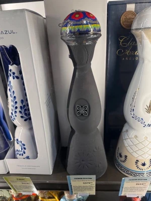 Svart dekorativ flaska med pärlhuvud - Unik svart dekorativ flaska från Clase Azul med en färgglad pärlprydd topp i blått, rött, gult och grönt. Flaskans kropp har ingraverade blommönster och en elegant, smal form. Perfekt som samlarobjekt eller inredningsdetalj.