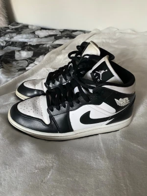 Svarta och vita Air Jordan 1 Mid - Snygga Air Jordan 1 Mid i svart och vitt. De är använda en del och har en liten gul miss färgning på flärpen som syns på bild 2 & 5. Även crease som syns på bild 4 och slitage på sulan under på bild 3. Hör av er vid frågor. Har beställt de på Zalando och beställningen syns på mitt konto där!