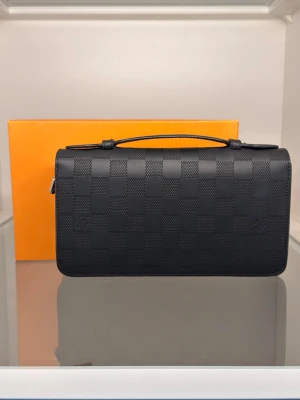 Black Checkered Zip Clutch - A refined, all-black structured clutch designed for a clean and elevated look. With its compact size (approx. 20 × 12 cm), it sits perfectly between a wallet and a small bag — giving you enough space for daily essentials while maintaining a slim, structured profile. 
