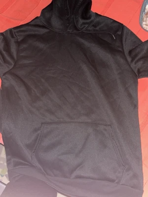 Svart hoodie med tryck från XING - Svart hoodie med stor ficka framtill och huva med dragsko. Baksidan har ett färgglatt tryck med texten 'MAKE MONEY NOT FRIEND' och motiv av blomma, jordglob och krona. Materialet är mjukt och lite glansigt, perfekt för en avslappnad streetwear-look. Storlek finns i s och m 