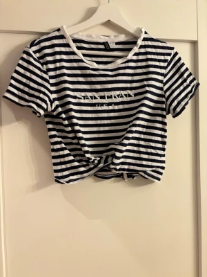 Randig croppad t-shirt SAN FRAN - Snygg croppad t-shirt från H&M med marinblå och vita ränder. Tryck med texten 'SAN FRAN USA' på bröstet. T-shirten har korta ärmar, rund halsringning och är gjord i mjuk bomull. Perfekt för en avslappnad och trendig look.