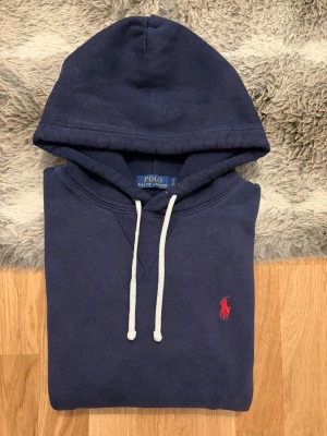 Marinblå Polo Ralph Lauren Fleece Hoodie - Storlek S - Hej! 👋 Säljer en riktigt snygg marinblå Polo Ralph Lauren hoodie i storlek S med röd logga. 🐎 Tröjan är i mycket gott skick och känns väldigt fräsch. Inga hål eller fläckar! ✨ 100% äkta med alla tvättlappar kvar. QR-koden finns och fungerar precis som den ska för enkel verifiering ✅ Ett perfekt premium-basplagg som kombinerar stil och kvalitet på bästa sätt. Passa på att fynda en klassiker i toppskick! Fraktar snabbt! 🚛📦💬💯 