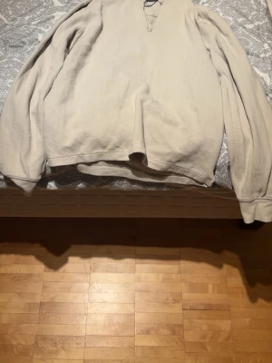Beige långärmad tröja med krage - En beige långärmad tröja med krage och halv dragkedja framtill. Tröjan har avslappnad passform och breda muddar vid ärmsluten. Perfekt för en chill och stilren look.