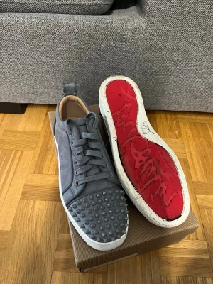 Gråa sneakers med nitar från Louboutin - Snygga gråa sneakers från Christian Louboutin med coola nitar på tån och klassisk röd sula. Storlek 40 och i befintligt skick. Tvättar innan frakt😇
