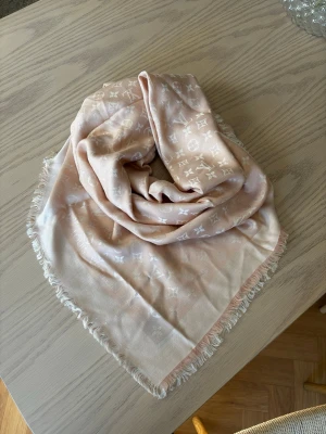 Ljusrosa sjal från Louis Vuitton - Snygg ljusrosa sjal från Louis Vuitton med klassiskt monogrammönster i ljusare nyans. Sjalens kanter har fina fransar och materialet känns mjukt och lyxigt. Helt i nyskick då den inte kommit till användning. Jag har köpt den i en vintage butik och har därför inget kvitto. 