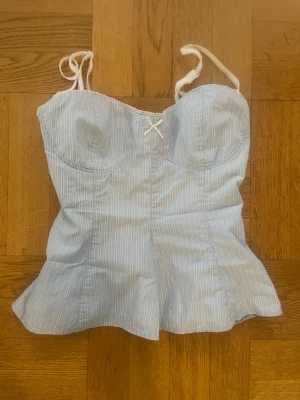 Ljusblått linne/korsettopp med rosett, från Zara - Jättefint linne från Zara i storlek M, men kan även passa vissa storlek S 💕 Linnet har en vacker form och ett vitt- och ljusblå randigt mönster, samt vita detaljer runt kanten på ringningen 🤍   Den är i perfekt skick! Nästan aldrig använd och har inga defekter.  Så fin till sommaren och att matcha till kjol såväl som jeans! 🌸