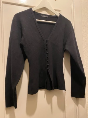 Svart kofta med knappar Gina Tricot - Snygg svart kofta från Gina Tricot i storlek XS. Modellen har v-ringning, långa ärmar och dekorativa knappar framtill. Materialet är stickat och koftan har en figurnära passform som ger en stilren look. 