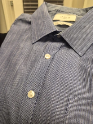 Blårandig skjorta från Jack's comfort fit M - Klassisk blårandig skjorta från Jack & Jones med vit knappstängning och bröstficka. Skjortan har lång ärm, krage och är tillverkad i bomull. Perfekt för en stilren look.
