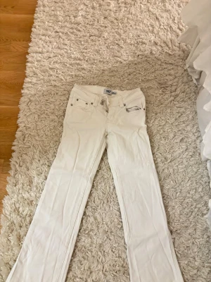 Vita bootcut jeans från 157 - Snygga vita bootcut jeans från 157 med klassisk femficksdesign och broderade detaljer på bakfickorna. Jeansen har låg midja och är tillverkade i ett stretchigt bomullsmaterial. Dom är storlek XS SHORT men jag är 164 och dom sitter perfekt i längden för mig!