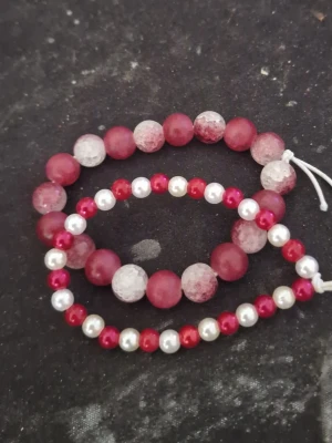 Rosa och vita pärlarmband - Två snygga armband med pärlor i rosa och vitt. Det ena armbandet har större, frostade rosa pärlor och det andra har mindre pärlor i rött och vitt. Båda är elastiska och passar de flesta handleder. Perfekt accessoar för att ge lite färg till din stil.