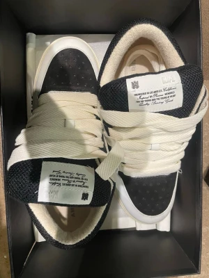 Svarta och vita sneakers från Amiri - Snygga sneakers från Amiri i svart och vitt med grova vita skosnören och mesh-detaljer. Skorna har Amiri-logga på sidan och tungan, samt en chunky sula för extra attityd. Tillverkade i en mix av läder och textil för en modern look. Storlek 44 pris kan diskuteras 