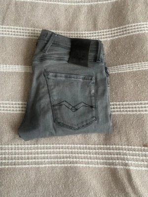 Gråa jeans från Replay - Snygga gråa jeans från Replay med klassisk femficksmodell och raka ben. Jeansen har en diskret logga på bakfickan och är tillverkade i mjukt denimtyg som ger en skön passform. Perfekta för dig som gillar en stilren och avslappnad look. Har ett litet hål i skrevet men inget man lägger märket till. 