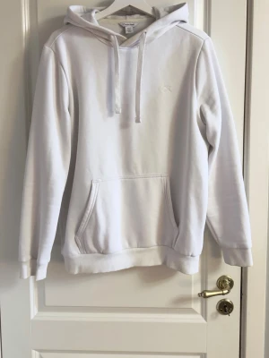 Vit hoodie från Calvin Klein - Snygg vit hoodie från Calvin Klein med broderad CK-logga på bröstet. Klassisk modell med huva och dragsnören samt stor magficka framtill. Tillverkad i mjukt bomullsmaterial och har ribbade muddar vid ärmslut och nederkant.