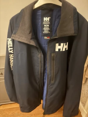 Marinblå Helly Hansen vindjacka - En blå helly Hansen jacka perfekt nu till våren och sommaren. Skicket är som ny(ej använd). 
