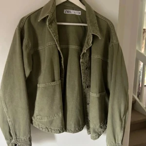 Grön jeansjacka Zara - Säljer en olivgrön jeansjacka från Zara. Jackan har två stora fickor framtill, klassisk krage och knappar längs hela framsidan. Perfekt att slänga på sig över en hoodie eller t-shirt för en chill look.