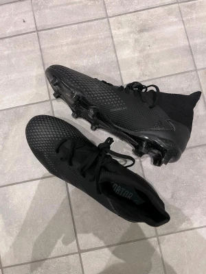 Adidas Demonscale Predator, 42,5 - Riktigt fina svarta fotbollsskor säljes för utomhusboll. Storlek 42,5 US 9. Endast använda ett fåtal gånger, dobbarna och skorna överlag är 9/10 skick. 
