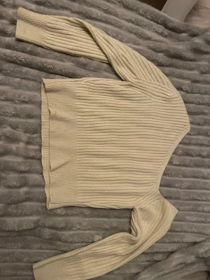Beige ribbstickad tröja - Säljer en beige ribbstickad tröja med lång ärm och rund halsringning. Tröjan har en klassisk, rak passform och breda ribbade muddar vid ärmslut och nederkant. Perfekt för lager-på-lager och enkel att matcha med olika outfits.okänt märke , känns som mindre M. Vit/beige