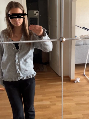 Ljusgrå kofta med volangkant - Söt ljusgrå kofta med volangkant och pärlknappar framtill. Koftan har långa ärmar och ribbstickade muddar. Perfekt att slänga över en topp för en chill look.