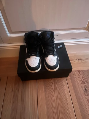 Air Jordan 1 Mid svart/vit/lila - Säljer ett par Air Jordan 1 Mid racer blue i svart, vitt och blått. Klassisk siluett med svart läder, vita paneler och blåa detaljer på häl och swoosh. Perforerad tåbox och svart snörning. Perfekta för dig som vill ha en ikonisk och stilren sneaker.