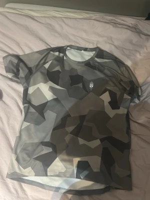 Kamouflage t-shirt från Försvarsmakten - Säljer en grå kamouflage t-shirt från Försvarsmakten med tryckt logga på bröstet och texten 'FÖRSVARSMAKTEN' på ryggen. Tillverkad i ett lätt och snabbtorkande syntetmaterial, perfekt för träning eller sportaktiviteter.!!! Svår att få tag på så där av priset men priset är ej hugget så kan sänka vid snabbt köp!!!! STORLEK L MEN PASSAR MIG SOM HAR MMEDIUM