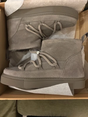 Gråa Inuikii classic low - KOSTADE 2500 KR! HELT NYA OCH KOMMER I ORGINAL FÖRPACKNING! SÄLJER EFTERSOM DE INTE PASSADE! Säljer ett par gråa Inuikii i mjuk mocka med fluffigt foder och grova snören. Skorna har en chunky sula och högt skaft som ger en riktigt cozy vinterlook. Perfekta för dig som vill ha både stil och värme under kalla dagar. SÄLJER ENDAST I 1-3 DAGAR SÅ PASSA PÅ! ANNARS LÄMNAR JAG TBX DEM