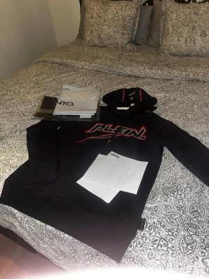 Svart hoodie från pp med tryck - Snygg svart hoodie från PLTN med stort färgglatt tryck på bröstet. Hoodien har huva med dragsko och röda detaljer, samt en klassisk känguruficka framtill. Perfekt för dig som gillar streetwear och vill sticka ut lite extra.