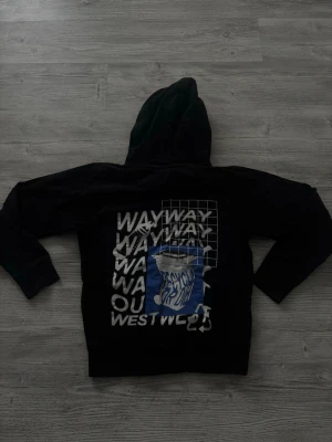 Svart hoodie med grafiskt tryck - Cool svart hoodie från Westwise med stor grafisk print i vitt och blått på ryggen och mindre tryck fram. Hoodien har en klassisk huva och ribbade muddar. Perfekt för dig som gillar streetwear och vill sticka ut med unika detaljer. Storlek S