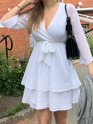 Vit omlottklänning med volanger - Supersöt vit kortklänning med omlott och knyt i midjan. Från Linn Ahlborgs kollektion hos Nakd 