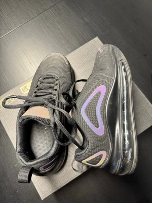 Svarta sneakers med lila detaljer - Säljer ett par svarta sneakers med lila och rosa detaljer samt transparent sula. Skorna har en sportig design med mesh-överdel och snörning. Perfekta för dig som gillar streetwear och vill ha en modern look.