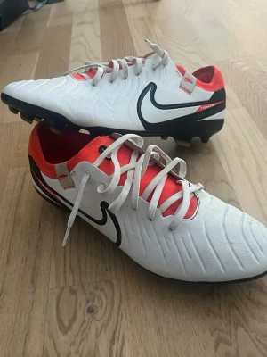 Nike Tiempo Legend 10 fotbollsskor vita FG ( Gräs) - Säljer ett par Nike Tiempo Legend 8 Pro fotbollsskor i vitt med svarta och röda detaljer. Skorna har klassisk snörning, tålig ovandel i syntetmaterial och dobbar för spel på gräs. Snygg design med stor svart Nike-logga på sidan och röd insida.Tveka inte på att ställa frågor 🤝