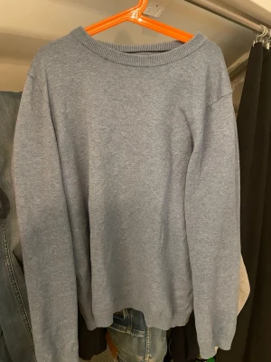 Ljusblå stickad tröja unisex MNG - En enkel och stilren ljusblå stickad tröja med rund halsringning och långa ärmar. Tröjan har ribbade muddar vid hals, ärmslut och nederkant. Perfekt att matcha med jeans för en avslappnad look.