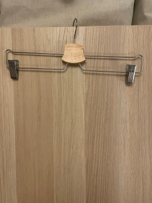 3 st Byxgalgar i metall och trä - Säljer ett gäng byxgalgar i metall med detaljer i ljust trä. Galgarna har klämmor i metall på båda sidor för att hålla byxor eller kjolar på plats. Snygg och stilren design som passar i de flesta garderober.