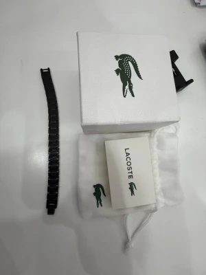 Svart metallarmband från Lacoste - pris kan diskuteras Snyggt svart armbandslänk från Lacoste i metall med graverad logotyp på spännet. Armbandet har en stilren och modern design med diskreta mönster på länkarna. Perfekt för dig som vill uppgradera din klocka med en exklusiv känsla.