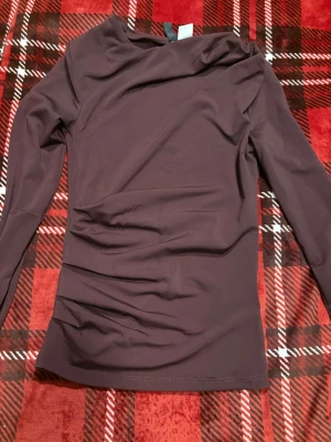 Vinröd topp från H&M Divided - Säljer en vinröd långärmad topp från H&M Divided. Toppen har en asymmetrisk halsringning och är figurnära i modellen. Tillverkad i mjukt stretchigt material som känns bekvämt mot huden. Perfekt att styla med jeans eller kjol.