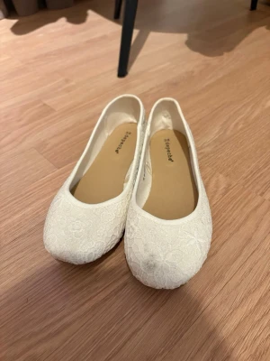 Vita spetsballerinaskor från Skopunkten - Säljer ett par vita ballerinaskor från Skopunkten med vacker spetsdetalj över hela skon. De har rund tå och en klassisk, låg profil som passar till många olika stilar. Perfekta för dig som gillar romantiska och feminina skor.  Finns även på Vinted 
