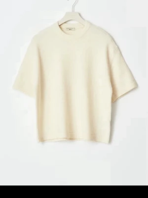 Krämvit stickad t-shirt - Säljer en krämvit stickad t-shirt från Gina med korta ärmar och rund hals. Tröjan har en boxig, avslappnad passform och är gjord i mjukt stickat material som känns lyxigt. Perfekt att styla med jeans eller kjol för en clean look.