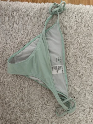 Mintgrön bikiniunderdel med knyt M - Snygg mintgrön bikiniunderdel med knyt i sidorna. Tillverkad i mjuk och stretchig polyesterblandning som sitter skönt på kroppen. Perfekt för lata dagar på stranden eller poolen. Knappt använd
