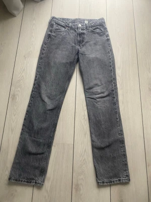 Grå raka jeans med vintagekänsla - Säljer ett par grå straight jeans med rak passform och klassisk femficksdesign. Jeansen har en snygg tvättad look och normal midja. Materialet är denim i bomull och de har en tidlös vibe som passar till det mesta. Perfekta för dig som gillar en avslappnad men stilren stil.