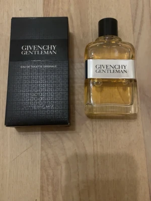Givenchy Gentleman Eau de Toilette - Givenchy Gentleman Eau de Toilette är en klassisk herrparfym i en stilren, transparent glasflaska med svart kork och vit etikett. Doften har en elegant och maskulin karaktär, och flaskan levereras med original svart kartong med Givenchy-logga. 100 ml 